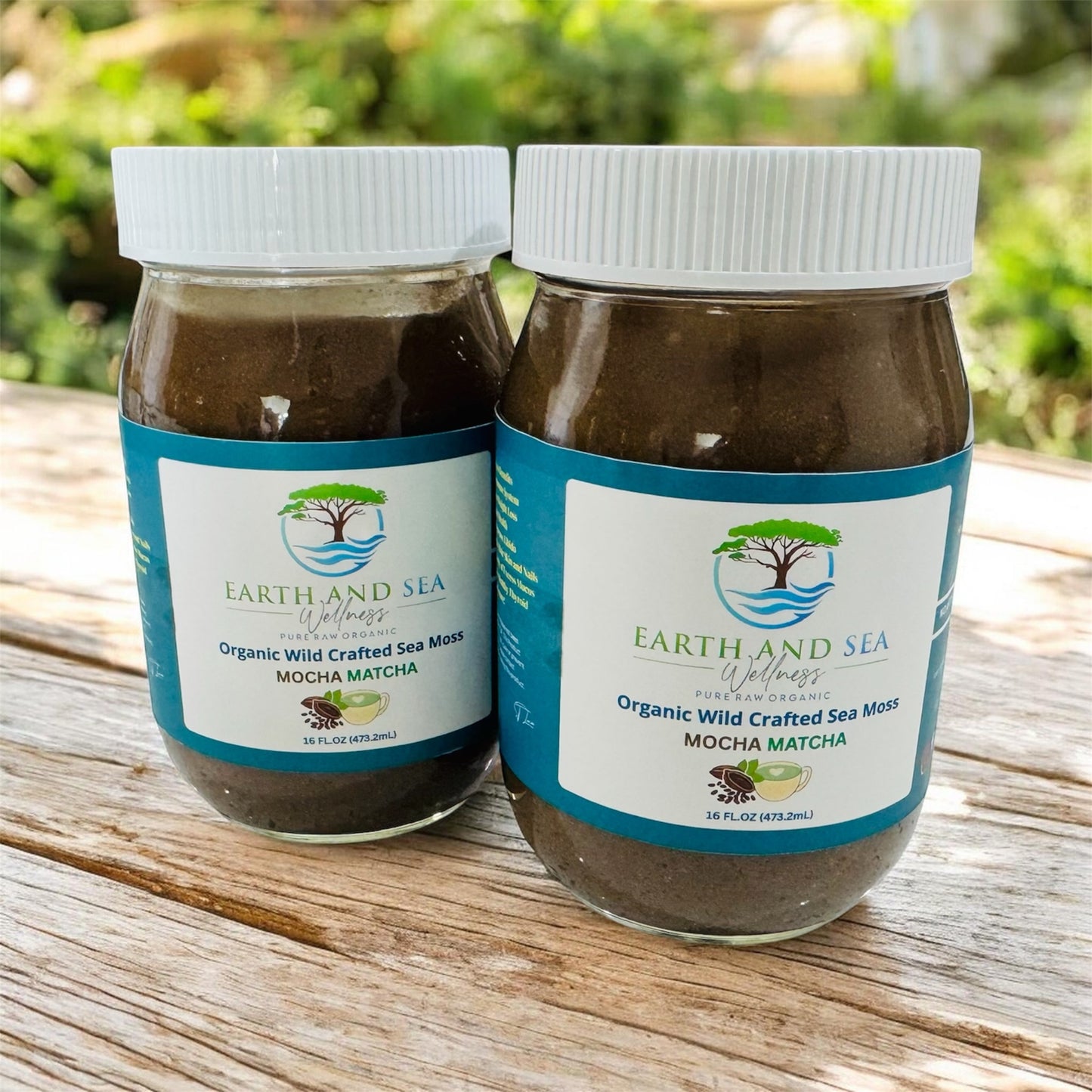 Two jars of Earth and Sea Wellness Organic Wild Crafted Sea Moss Mocha Matcha on a wooden surface with a blurred green background.
